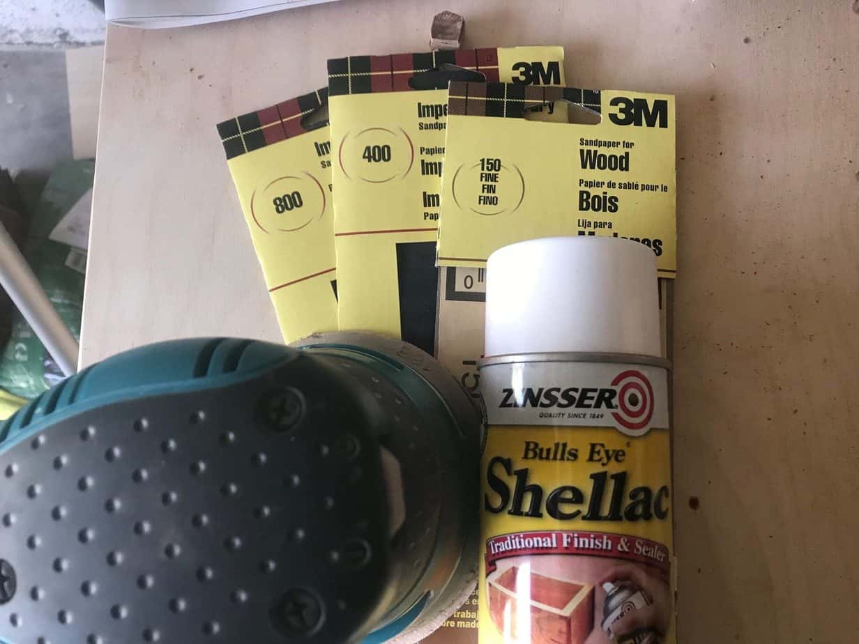 photo of three types of sandpaper and a spray bottle of shellac.