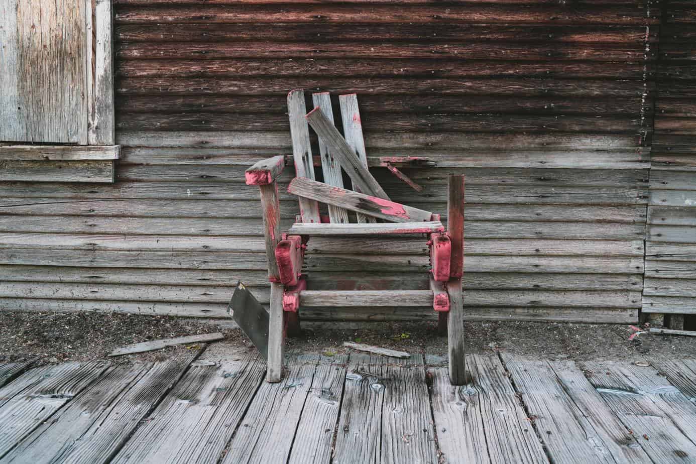 photo of a old broken wood chair on a old work wood deck and wall.