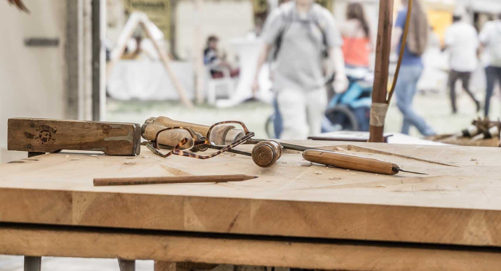 photo of a workbench with some marking tools on it and an old pair of glasses with people walking around in the background.