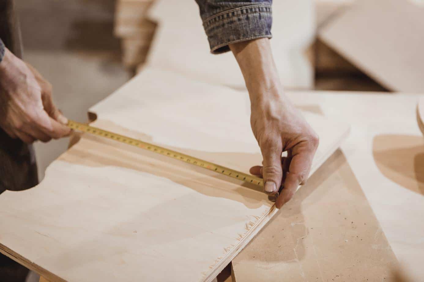 photo of a man measuring a board with a tape measure.